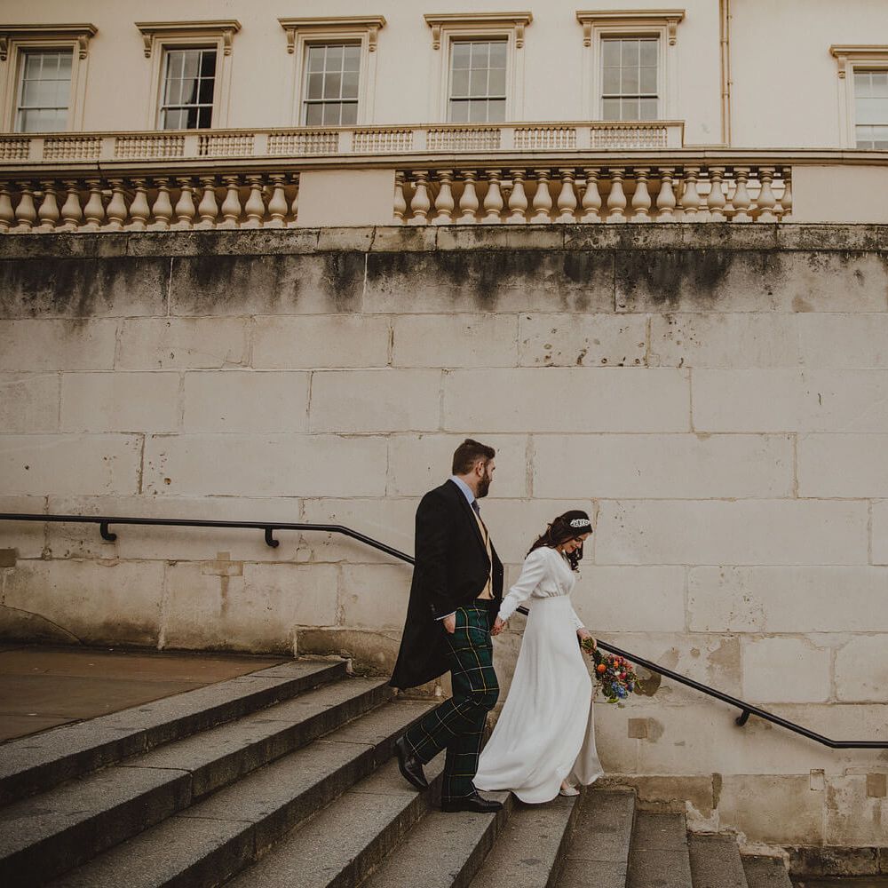 Bride and groom walking down steps, bride wears silk gown holding bright wedding bouquet