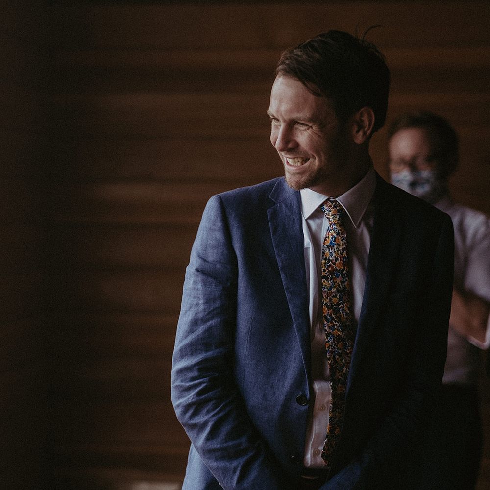 Groom smiles on the day of his wedding as he wears blue suit
