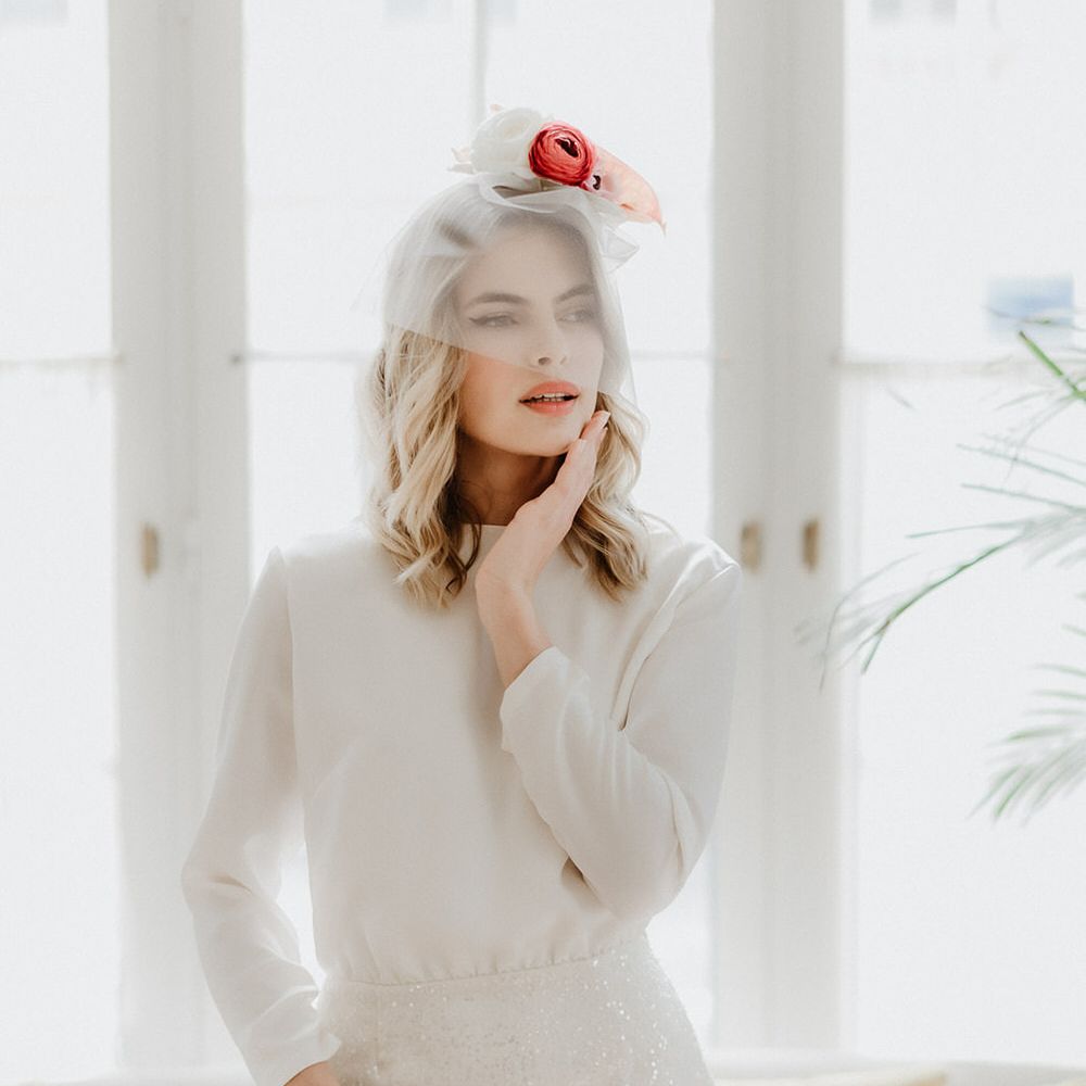 Bride wearing a long sleeve mid length wedding dress with sequin skirt detail, and a short mesh veil covering her face with flowers on her head