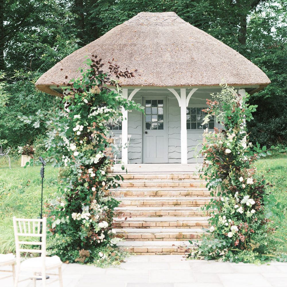 Outdoor wedding ceremony at Deer Park in Devon with vertical wedding flower arrangements decorating the altar