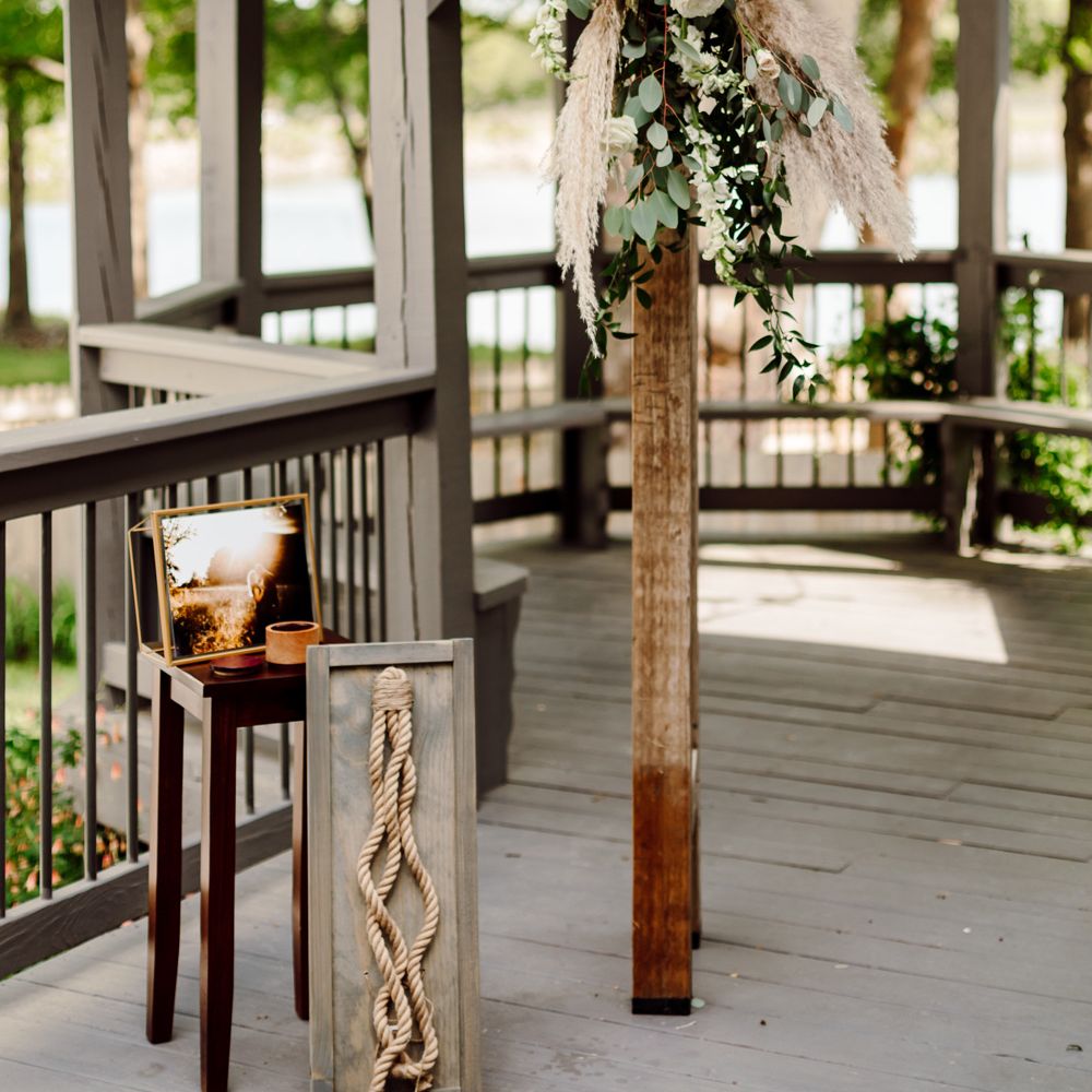 Wooden covered veranda with circular roof with white and green floral installation, knot for knot tying ceremony and table with couples photo on for backyard wedding