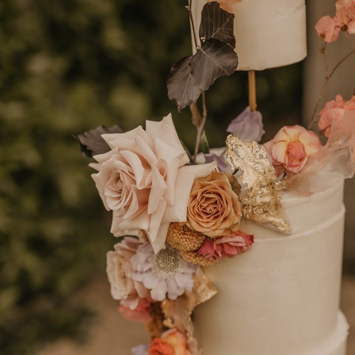 Buttercream wedding cake with elevated tier decorated in gold leaf and pastel wedding flowers 