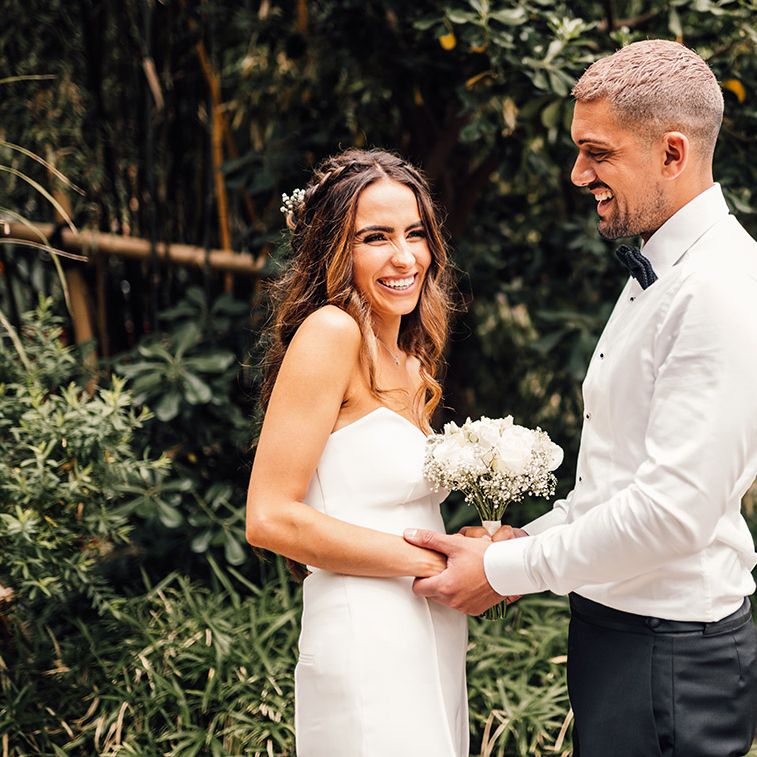 Groom in a white shirt and bow tie holding hands with his bride in a strapless bandeau top and trousers 