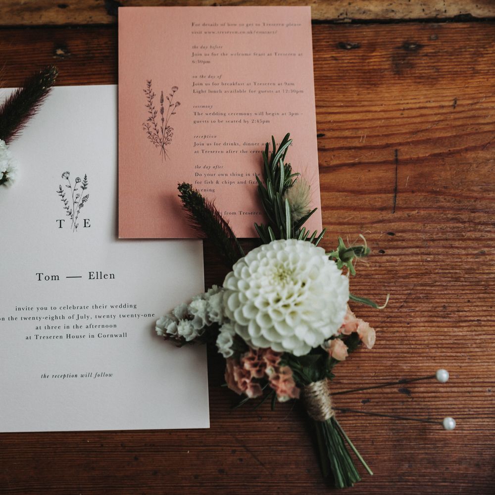 Simple wedding stationery complete in white and coral on a wooden table next to florals