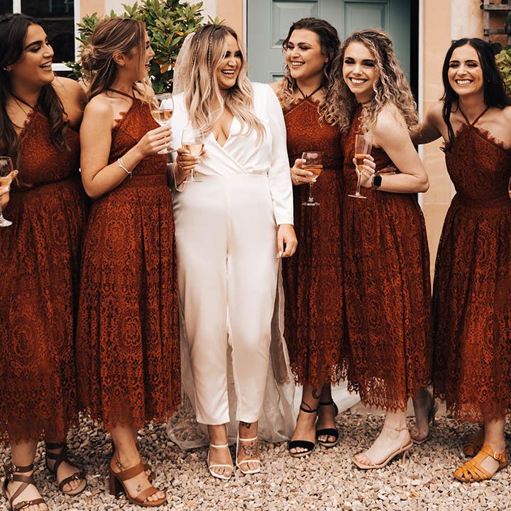 Bride stands with her bridesmaids who wear red dresses with lace and halter necks 