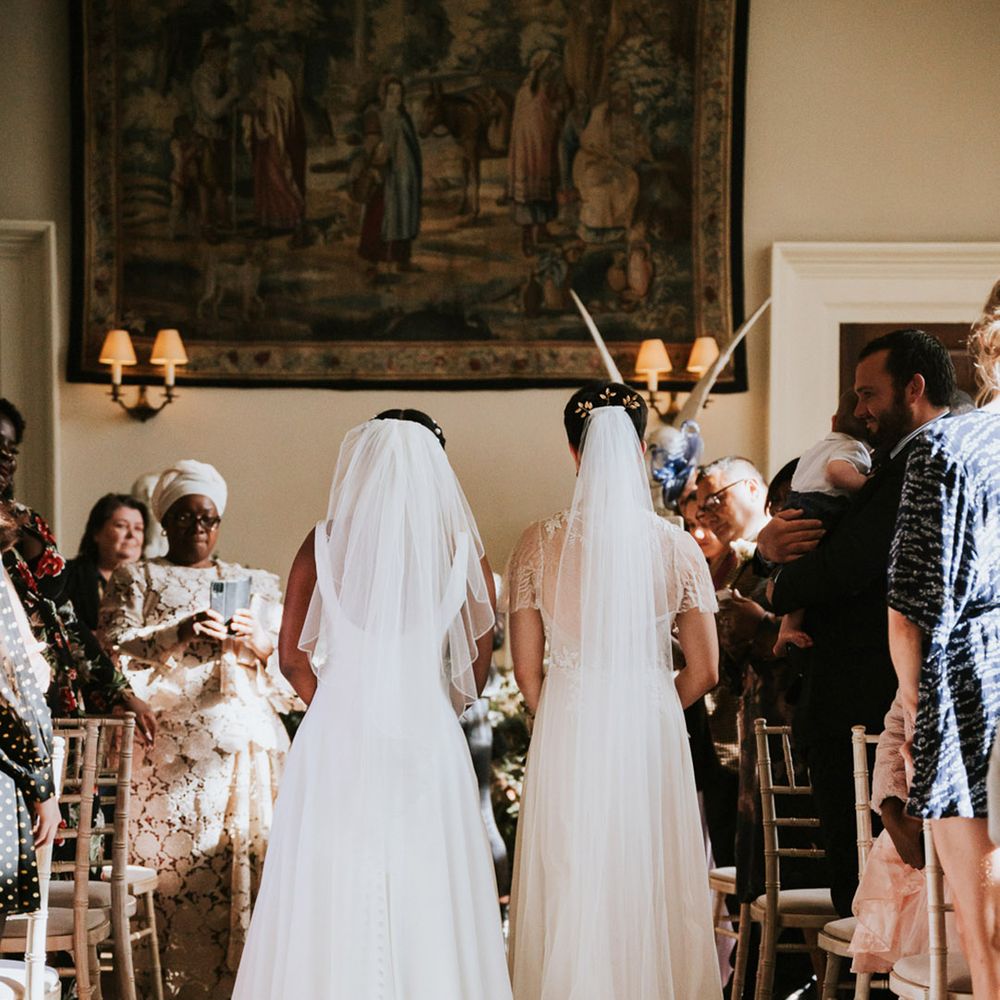 Two brides with long cathedral length veils walking down the aisle together at their Elmore Court wedding 