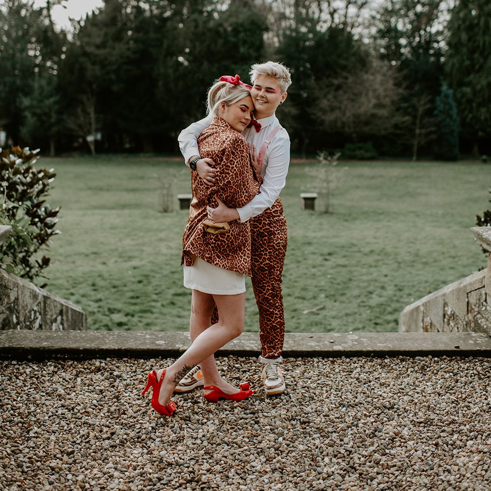 LGBTQ+ wedding with bride in a leopard bring suit embracing her bride in a short wedding dress with red bow shoes 