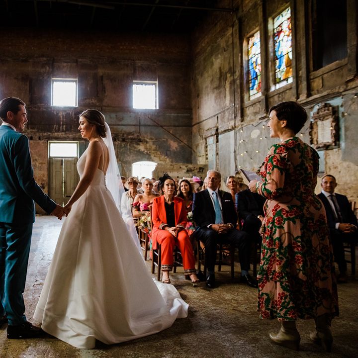 Wedding guests look on at the bride and groom at industrial venue with stained glass windows 