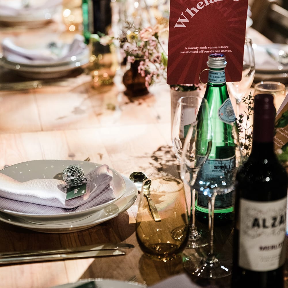 White plates with lilac napkins and name place cards with disco ball charm with red and white table name sign named after special places to the couple