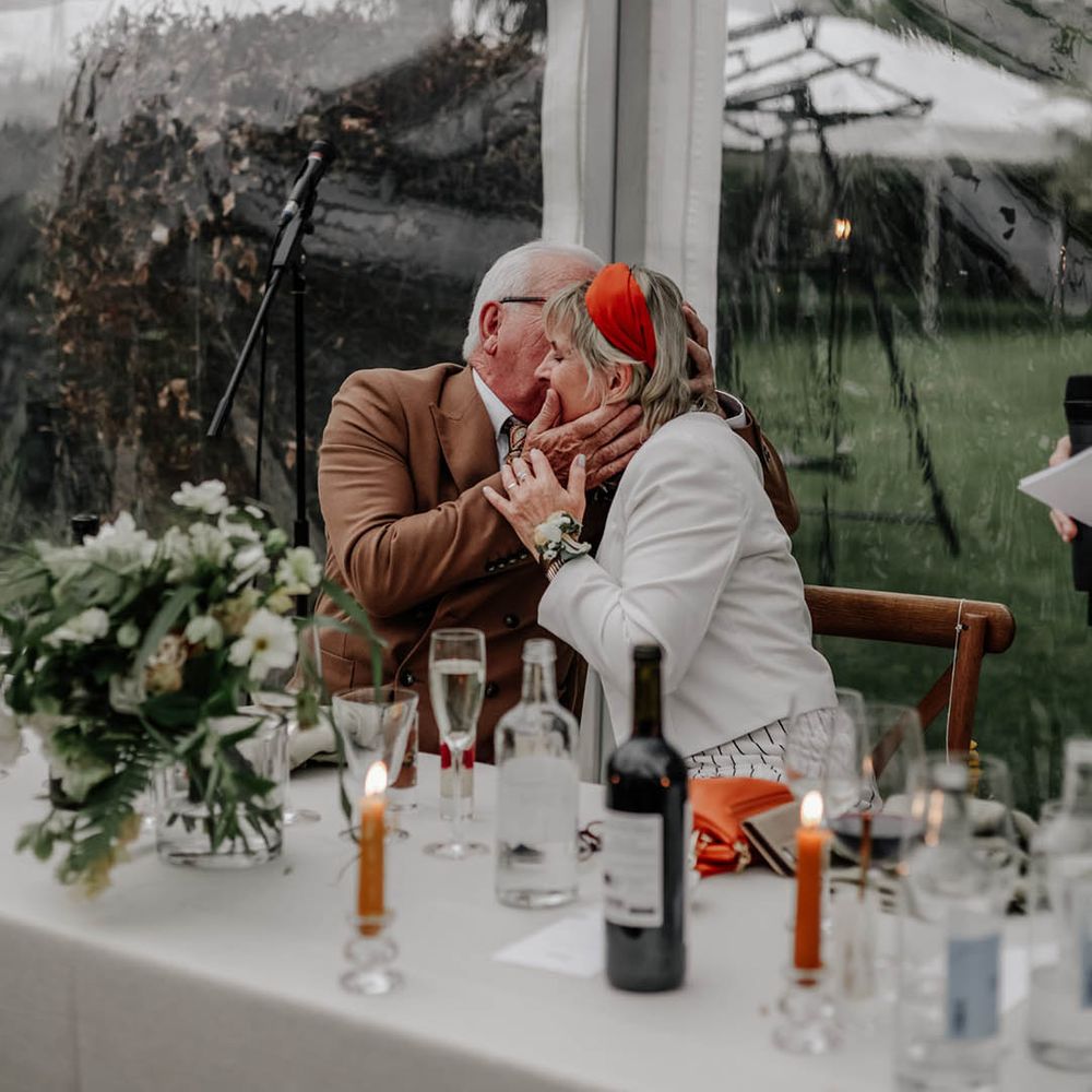 Father and mother of the groom kissing during the clear glass marquee reception 