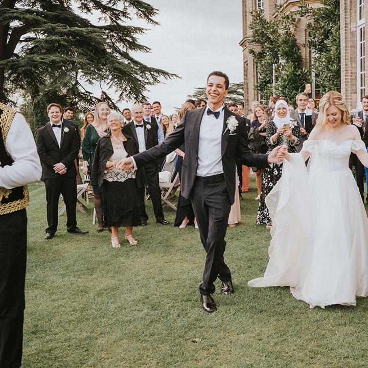 Bride in an off the shoulder wedding dress and groom in a tuxedo dancing in the grounds at Hedsor House with their Zaffa Band 