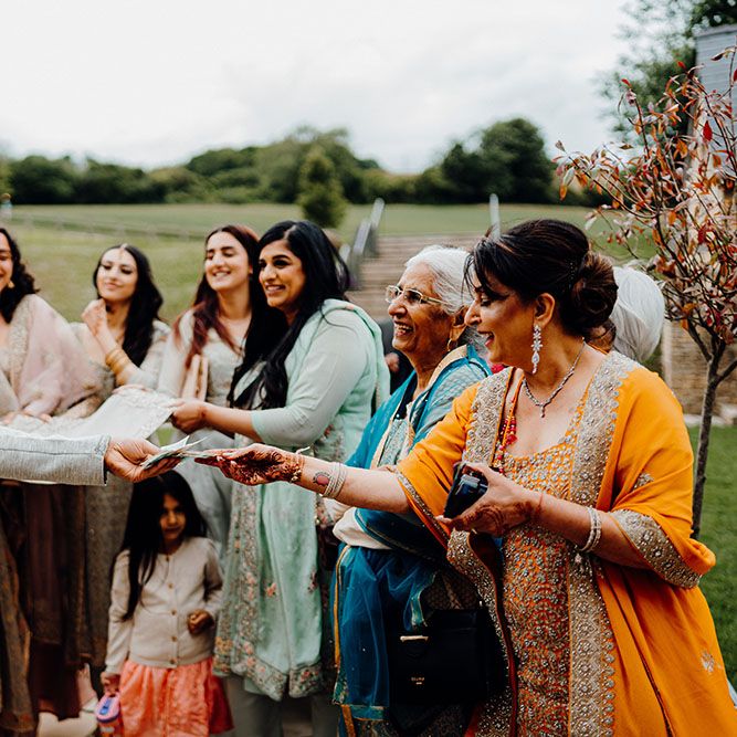 Groom wears traditional sherwani with embellishment whilst stood with wedding party who wear brightly coloured clothing for Nikkah ceremony