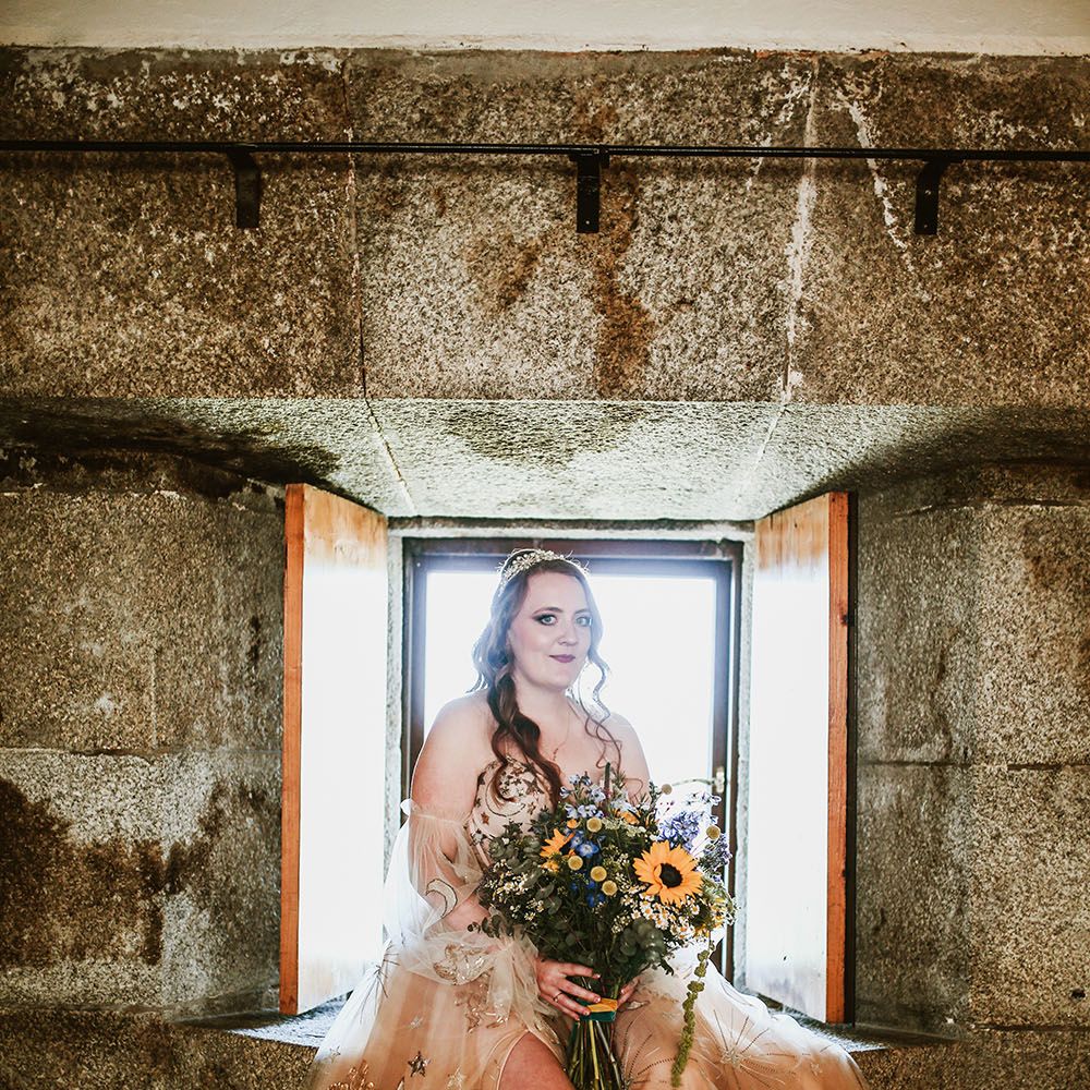 Bride wears pink starry wedding dress with off the shoulder sheer puffed sleeves and holds oversized floral bouquet with sunflowers and tied with green and orange velvet ribbon