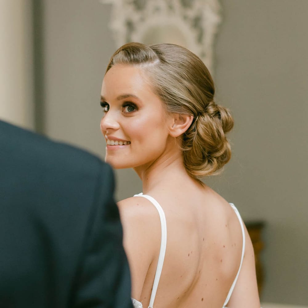 Bride smiles back at the groom as she wears her second off the shoulder outfit 