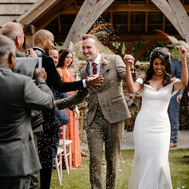 Groom high fives a wedding guest as confetti is thrown over them 
