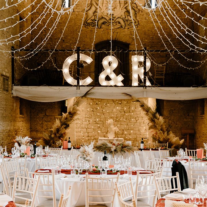 White circle tables with orange table runners with fairy lights, pampas grass and dried flowers with letter lights