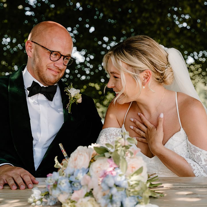 Bride & groom sign marriage certificate as they sit beside the bank of the River Thames