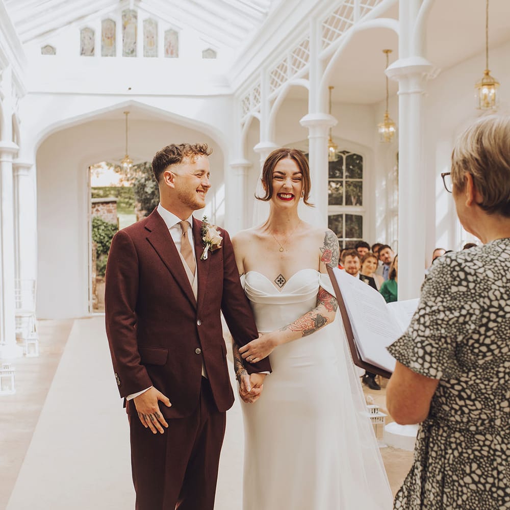 Bride in Vera Wang wedding dress stands with her groom in maroon suit on during wedding ceremony