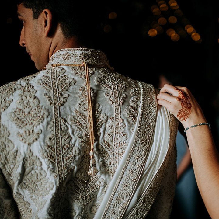 Groom wears beautifully embellished sherwani as guest helps him dress on the morning of his wedding day