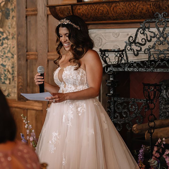 Bride with curled brown hair in a strapless tulle lace wedding dress and gold crown reading out her bridal speech