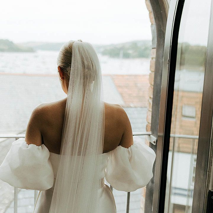 Bride wears floor length veil and Jesus Peiro wedding dress as she looks out toward the sea