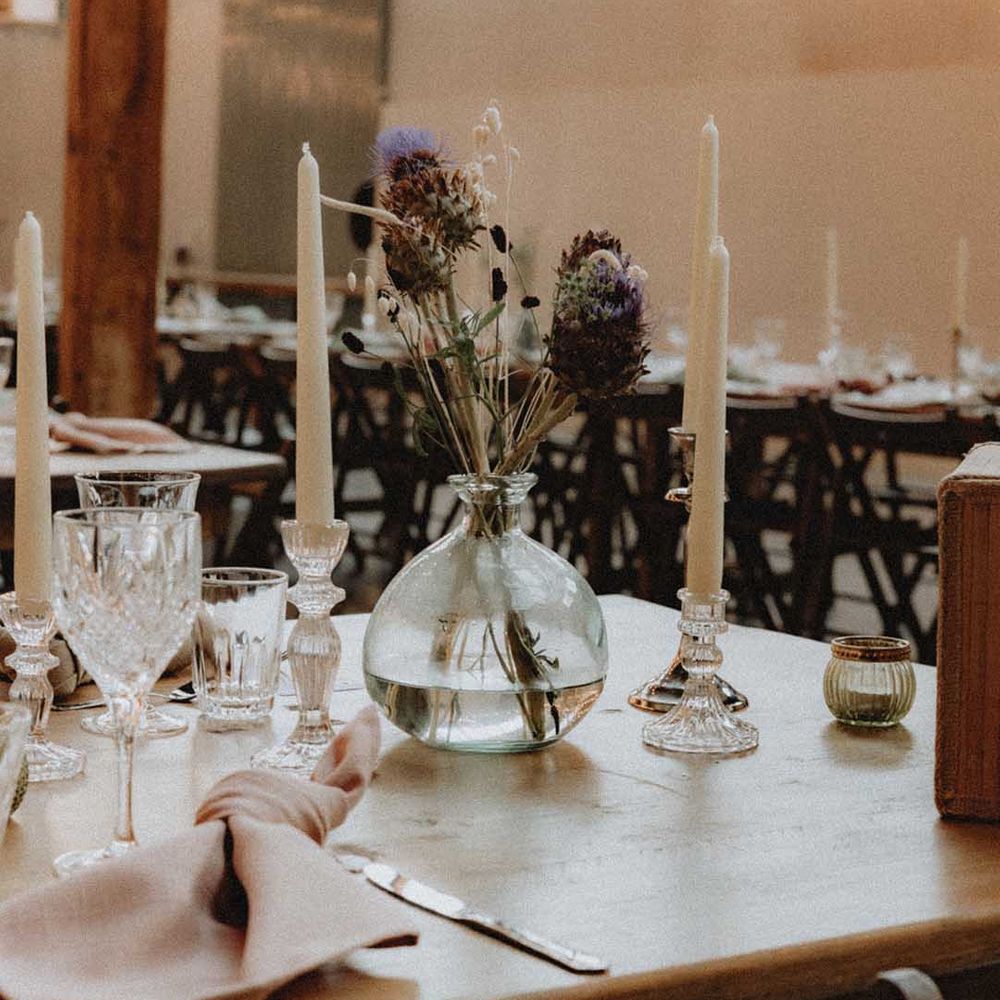 DIY wedding flower arrangements in glass vase beside white candles on wooden tables 