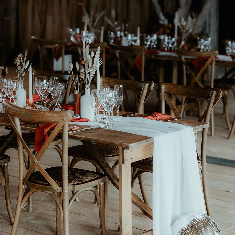 Rustic wooden table decorated with white table runners, burnt orange napkins and disco balls with bunny grass floral arrangements 