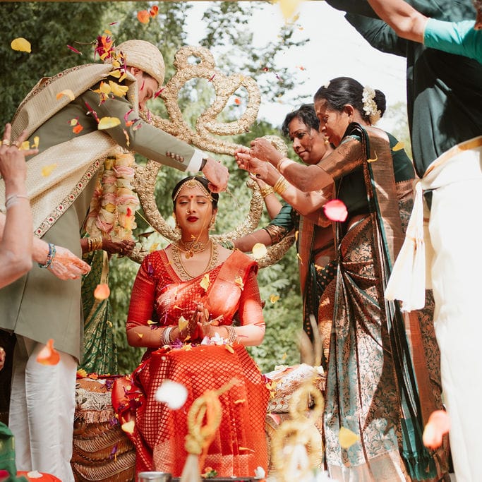 South Asian bride in a red legenga having petals sprinkled over her 