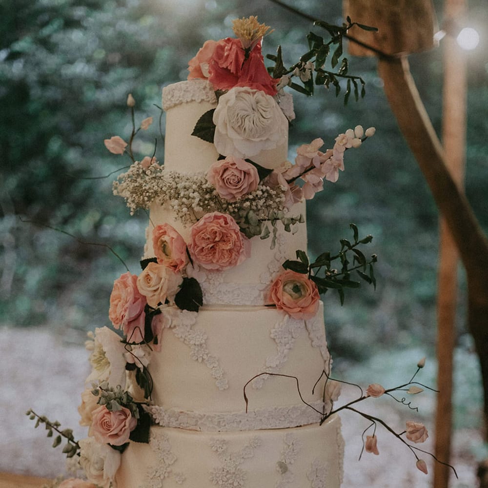 Four tier white wedding cake with pink and white flowers created with icing for outdoor woodland wedding 