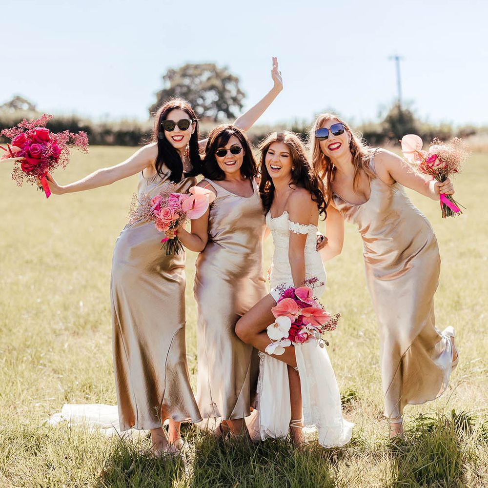 Bride in off the shoulder wedding dress posing with bridal party in gold satin bridesmaid dresses 