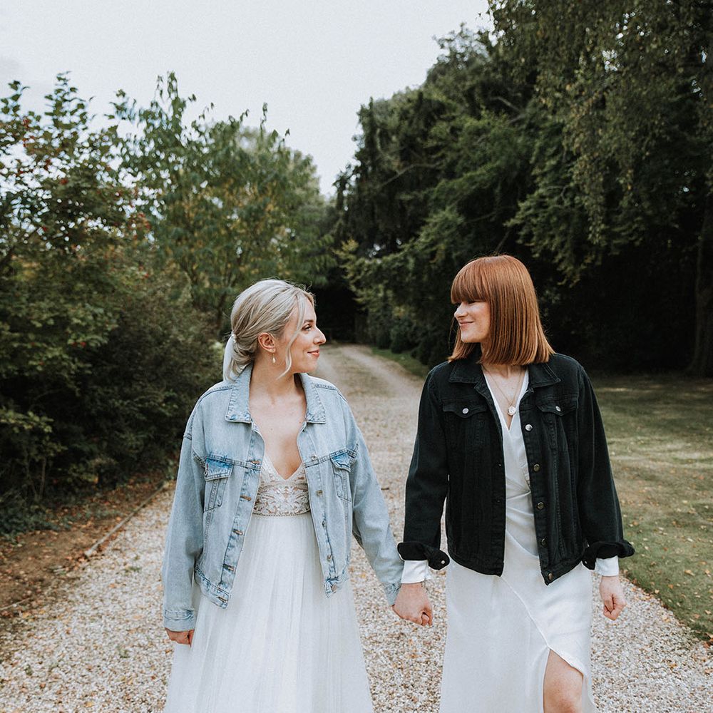 Bride in light blue denim jacket walking with bride in black denim jacket for LGBTQI+ barn wedding