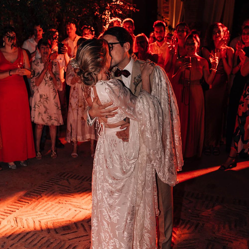The bride in bridal separates with the groom in cream suit have their first dance together 