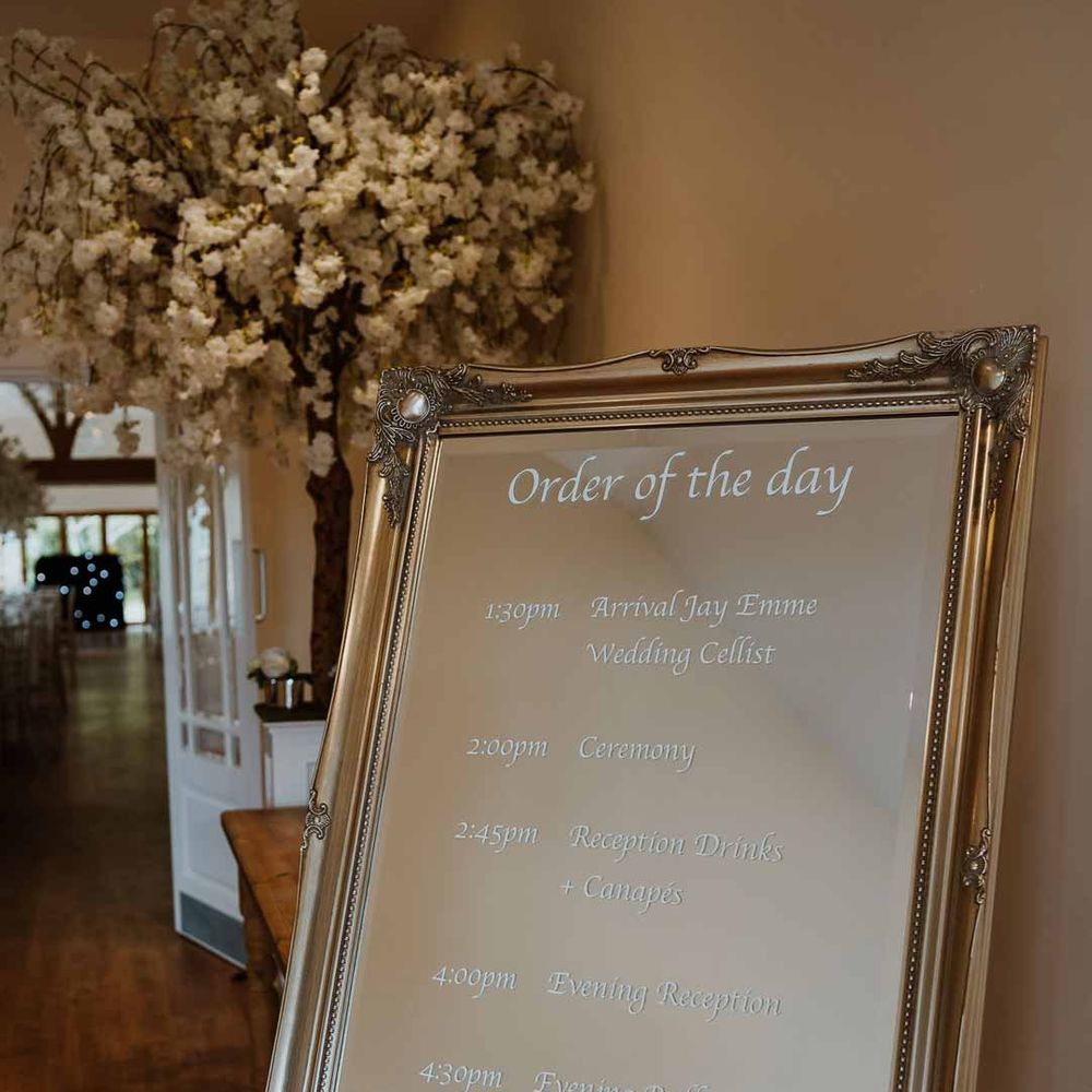 Mirrored order of the day wedding sign in gold frame on white easel at Tredudwell Manor 