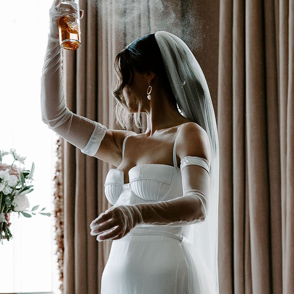 Bride in wedding dress and veil spraying wedding perfume 