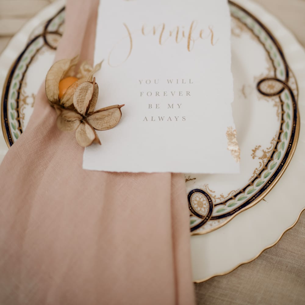 place setting with ornate tableware, natural linen and classic wedding stationery 