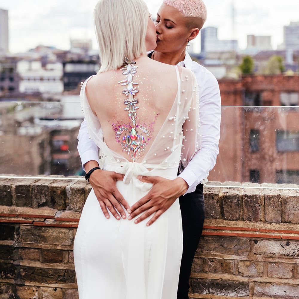 Bride with short hair kissing her bride with jewel body art on her back 