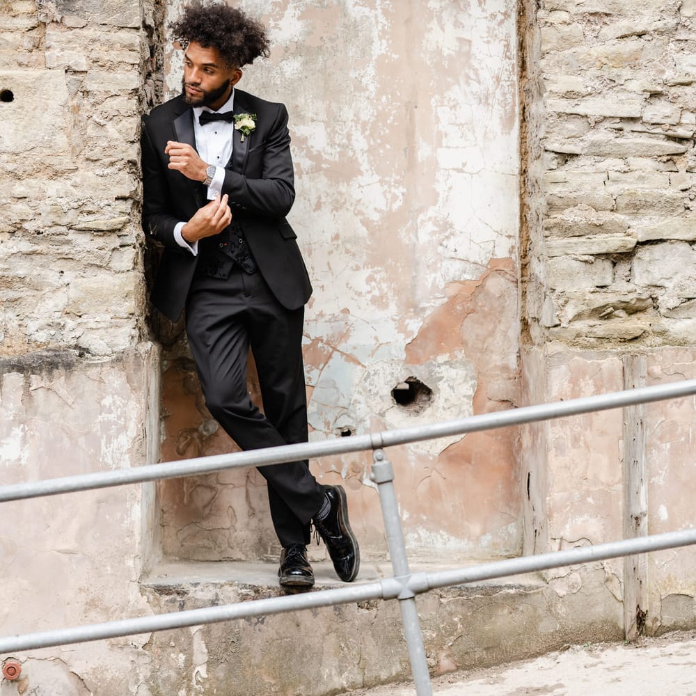 Stylish black groom with afro hair in a black tuxedo with bow tie and jacquard waistcoat 