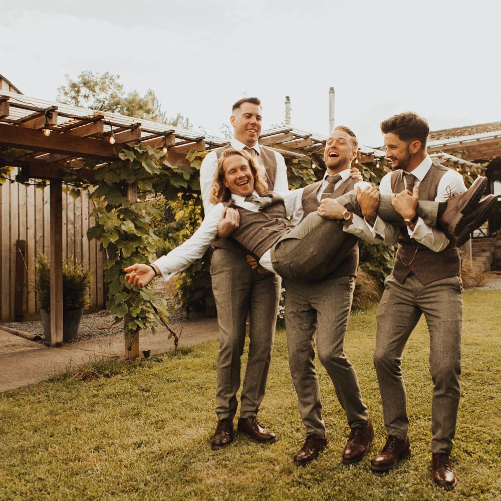 Three groomsmen in sage green trousers, waistcoats and ties hold groom in sage green trousers, waistcoat and tie in the garden at Anran Devon after wedding