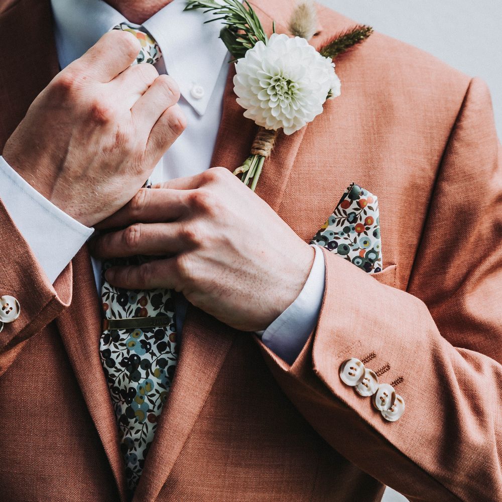 Groom does up his tie on wedding day as he wears floral buttonhole and colourful tie 