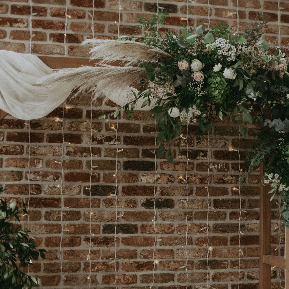 Flower cloud on wooden wedding arch with drapery in front of fairy string lights for Isle fo Wight wedding with macrame wedding decor