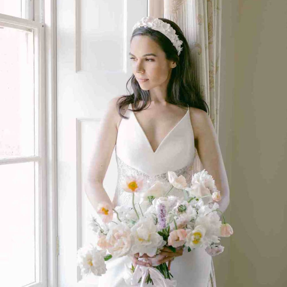 Bride in an A Line wedding dress with lace inserts and straps looking out the country house wedding venue holding a peony and rose wedding bouquet 
