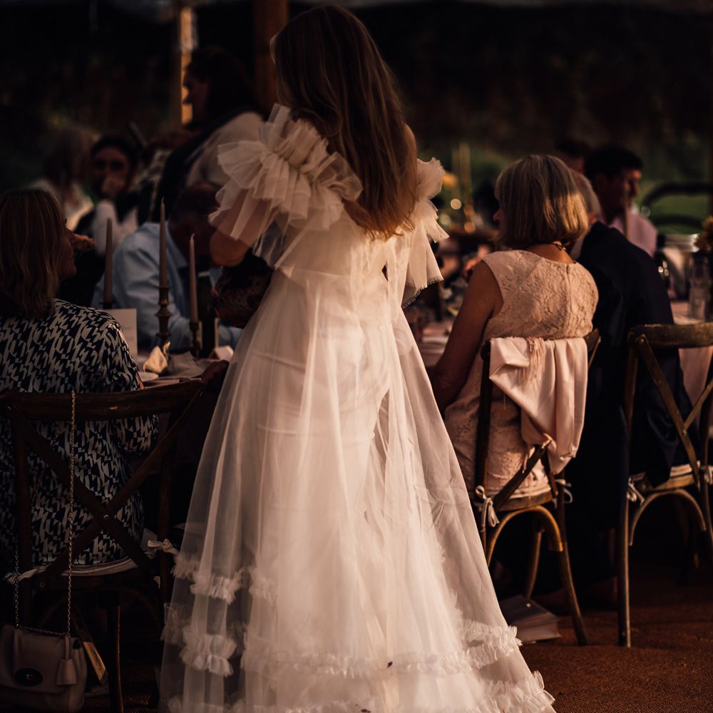 Bride in white Halfpenny London Mayfair dress stands in marquee during garden wedding reception in Cornwall