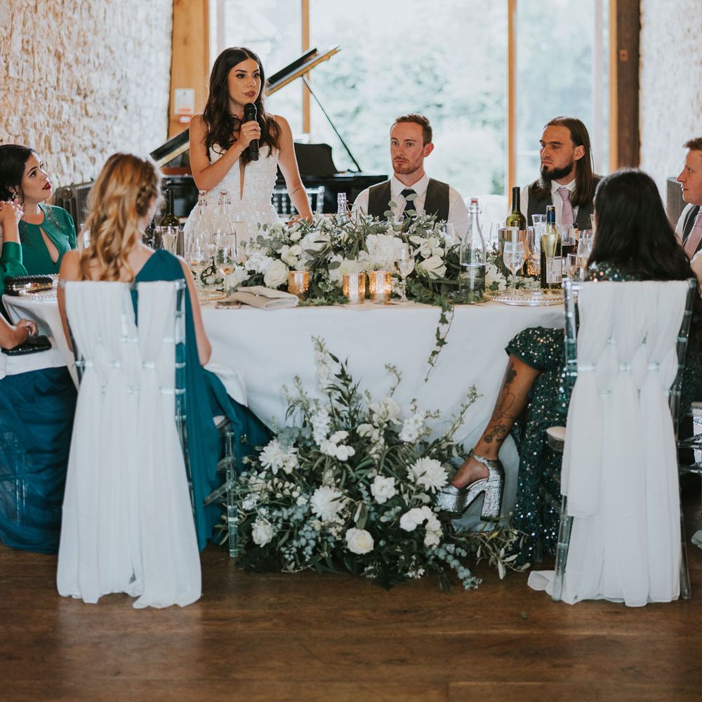 Bride in Pronovias wedding dress makes bride speech during wedding reception at Notley Abbey from round top table with groom, groomsmen and bridesmaids
