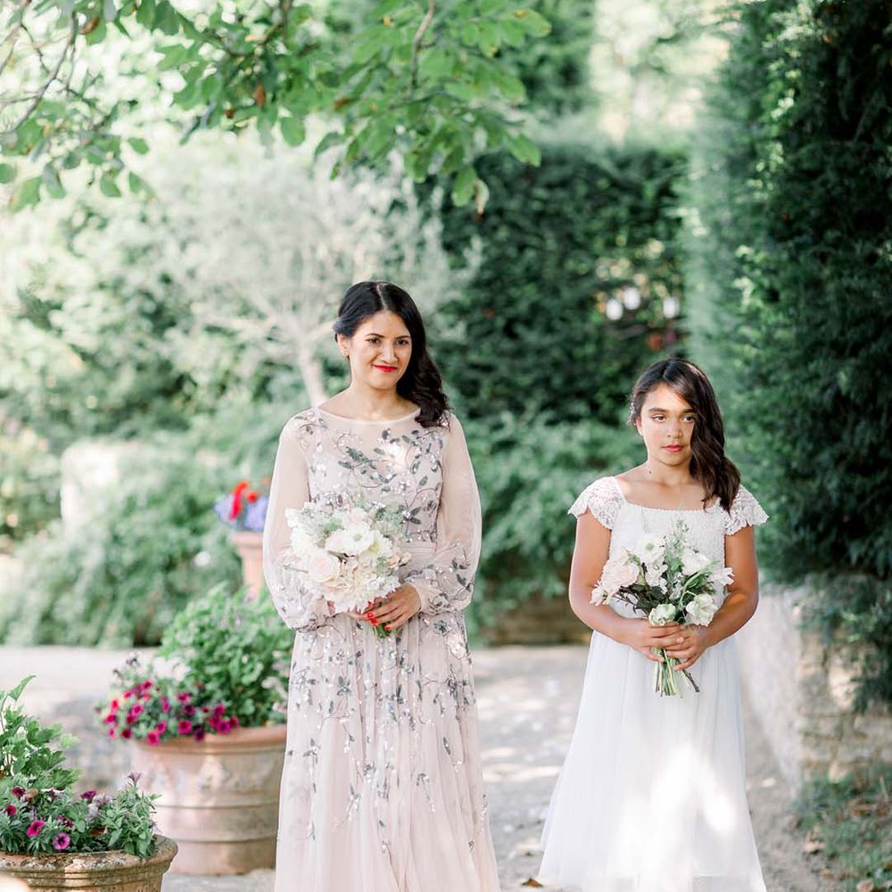 Bridesmaid walks with flower girl whilst holding floral bouquets 
