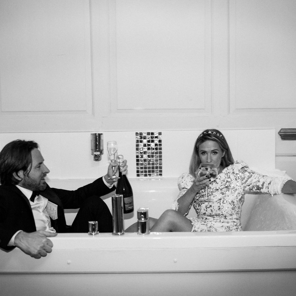 Bride & groom sit in bathtub on their wedding day in black & white image 
