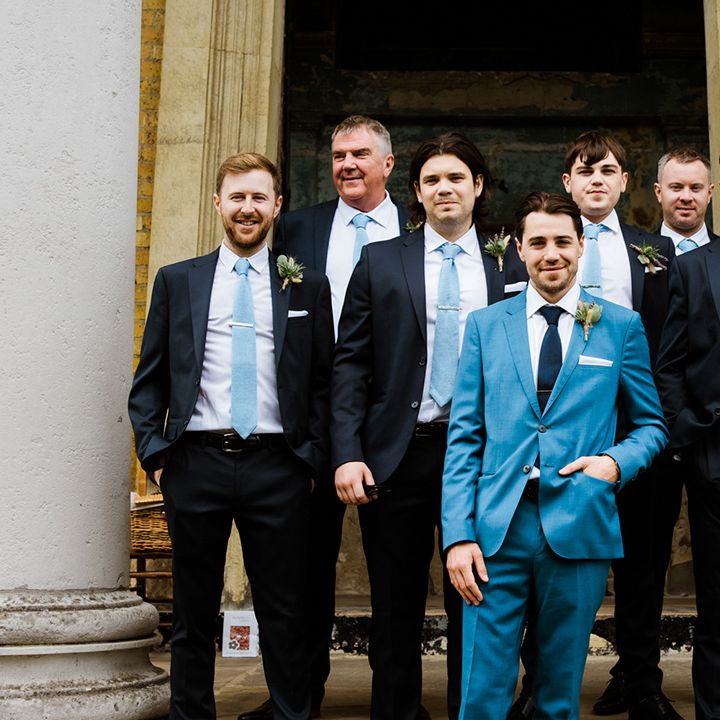 Groom in blue suit and black tie poses with groomsman in black suits and pale blue ties