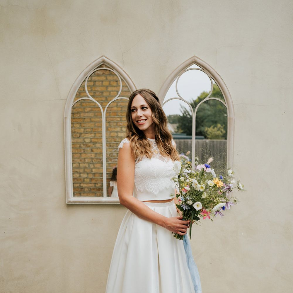 Bride in wedding lace top and high low skirt holding wildflower wedding bouquet tie with pale blue ribbon 