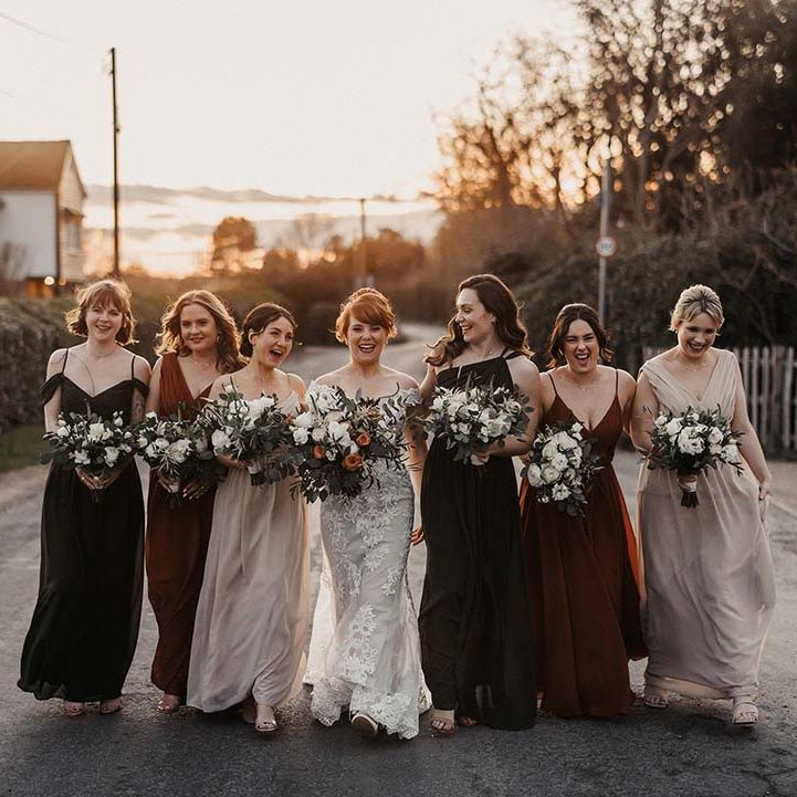 Laughing bride and bridesmaids walk along the road as golden hour hits