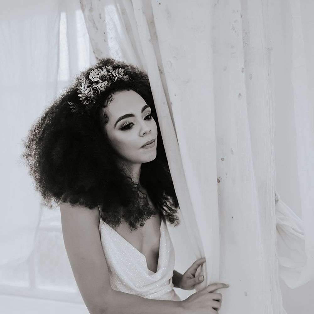 Black bride in a sparkly wedding dress with cowl front with naturally curly afro hair and hair accessory