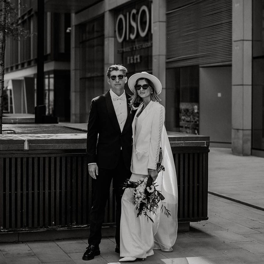 Bride and groom pose together wearing their sunglasses and suits for town hall wedding